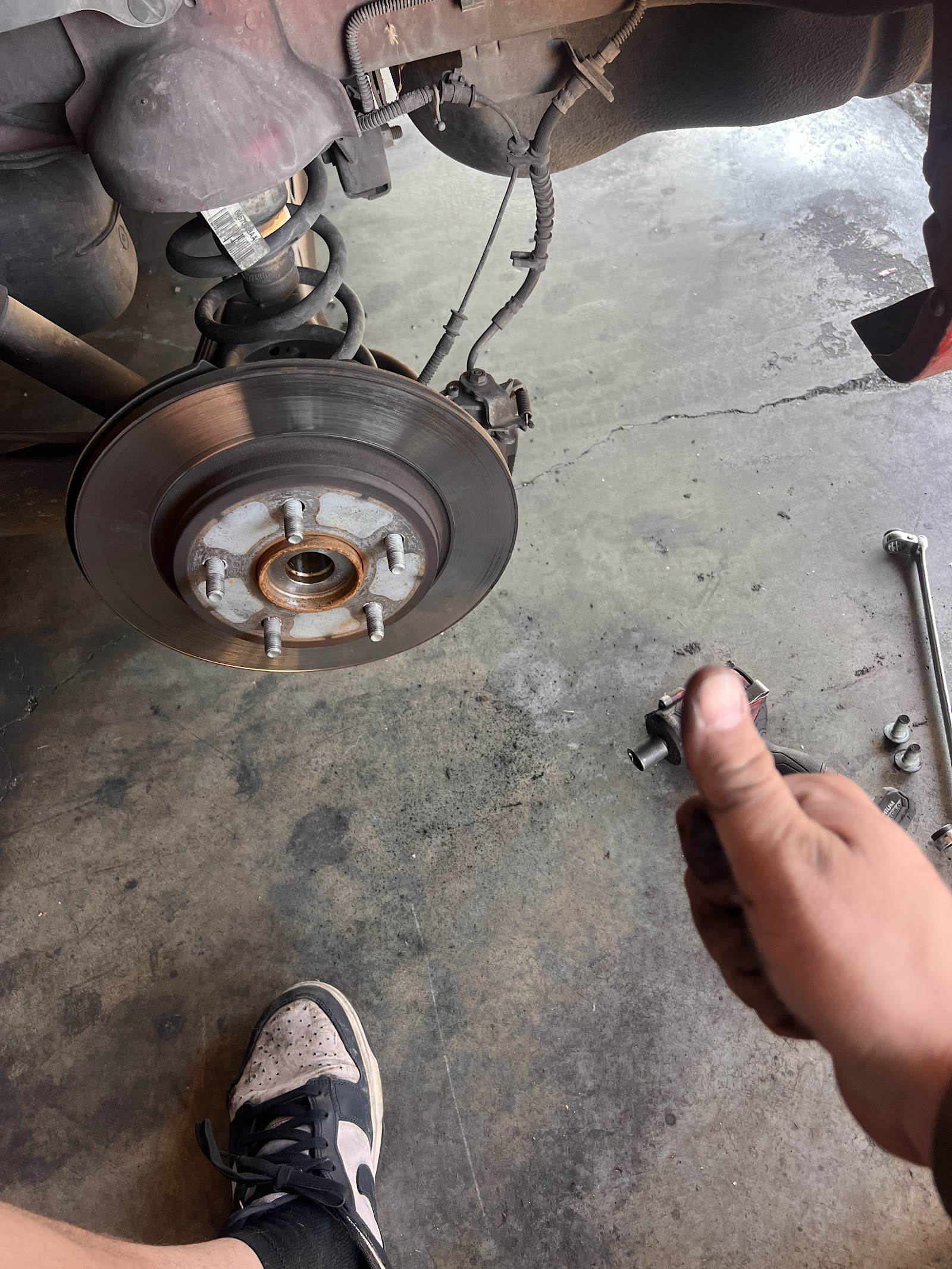 Mechanic holding a removed suspension component next to an exposed rear brake rotor and hub