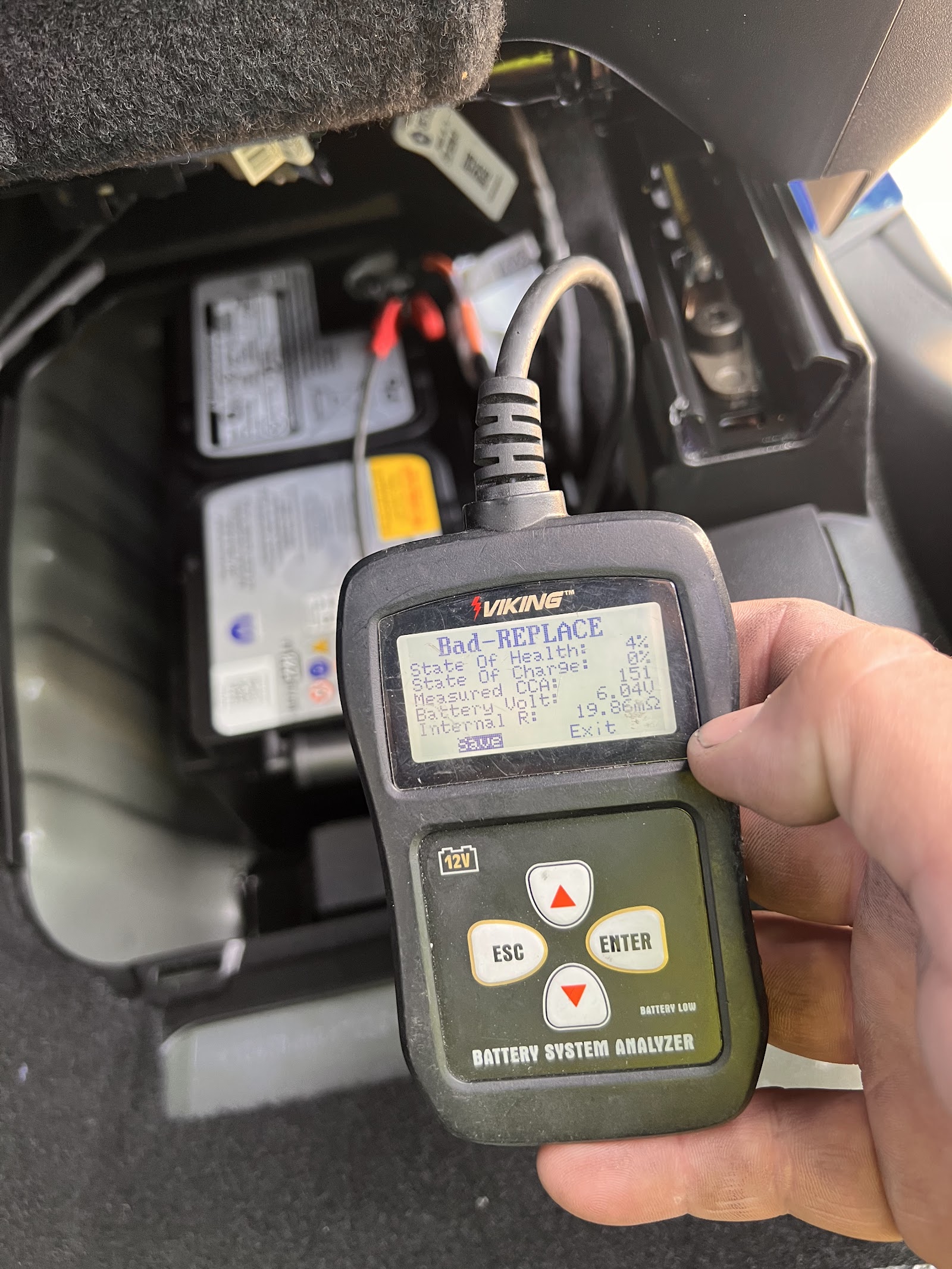 Battery analyzer displaying a 'Bad-REPLACE' result held near a vehicle battery