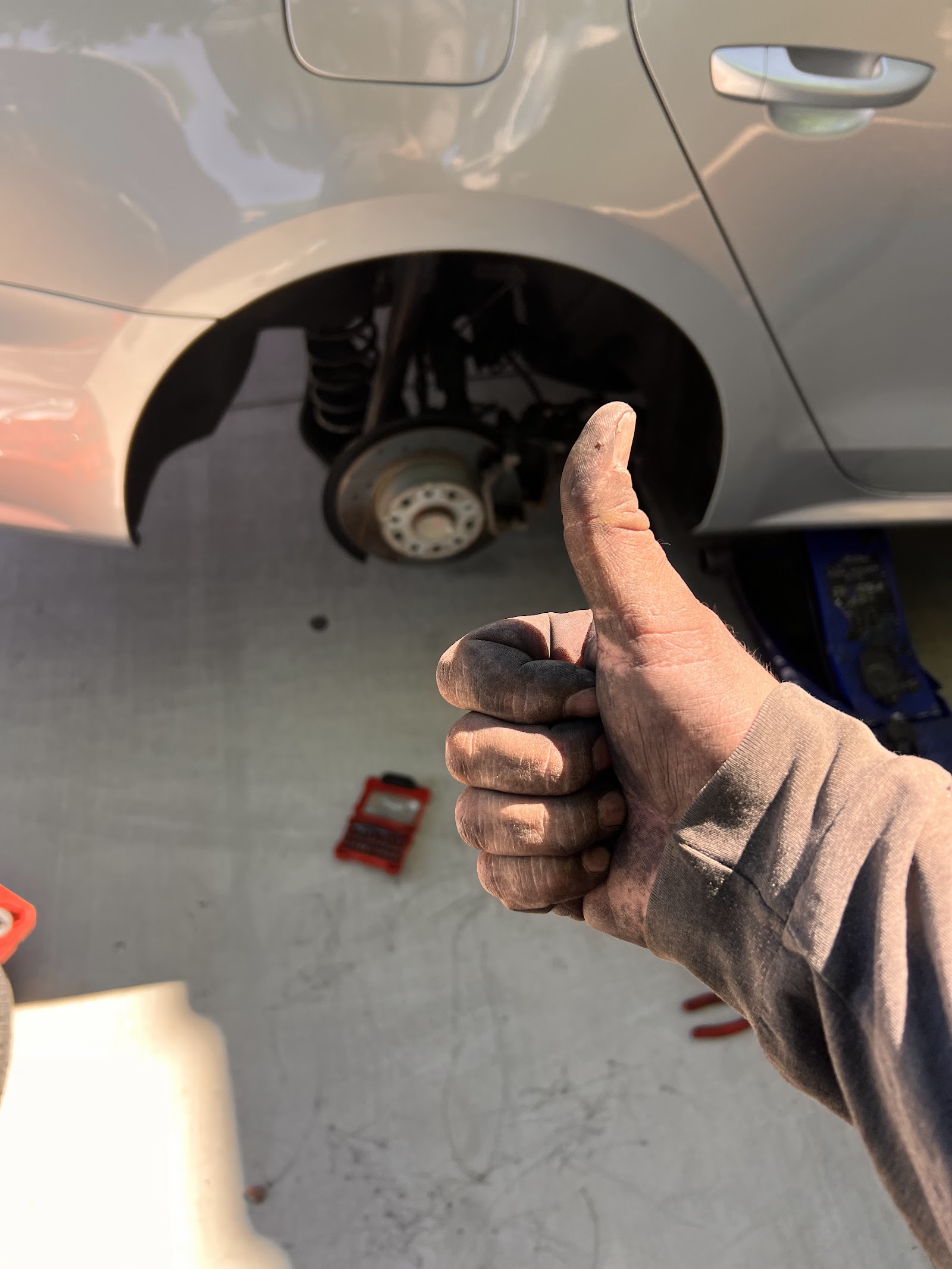 Mechanic's dirty hand giving a thumbs up next to a car with a wheel removed
