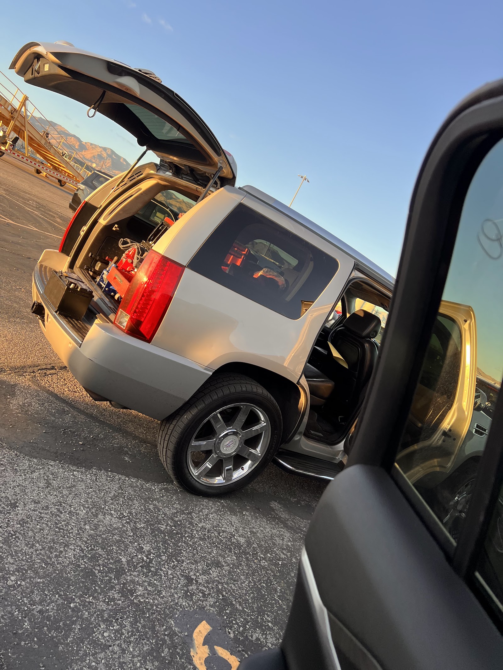 Cadillac Escalade with rear hatch open, loaded with tools at sunset in a parking lot